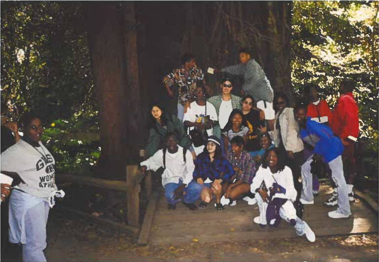 Students sitting in front of tree smiling at the camera